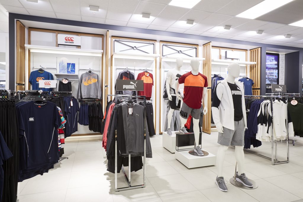 HOL Group A retail store showcases athletic wear. Mannequins display sporty outfits, including T-shirts, jackets, and shorts from brands like Puma and CCC. Clothing racks around the store hold more apparel, all brightly lit and neatly organized—a perfect place for farmers looking to upgrade their casual wardrobe.