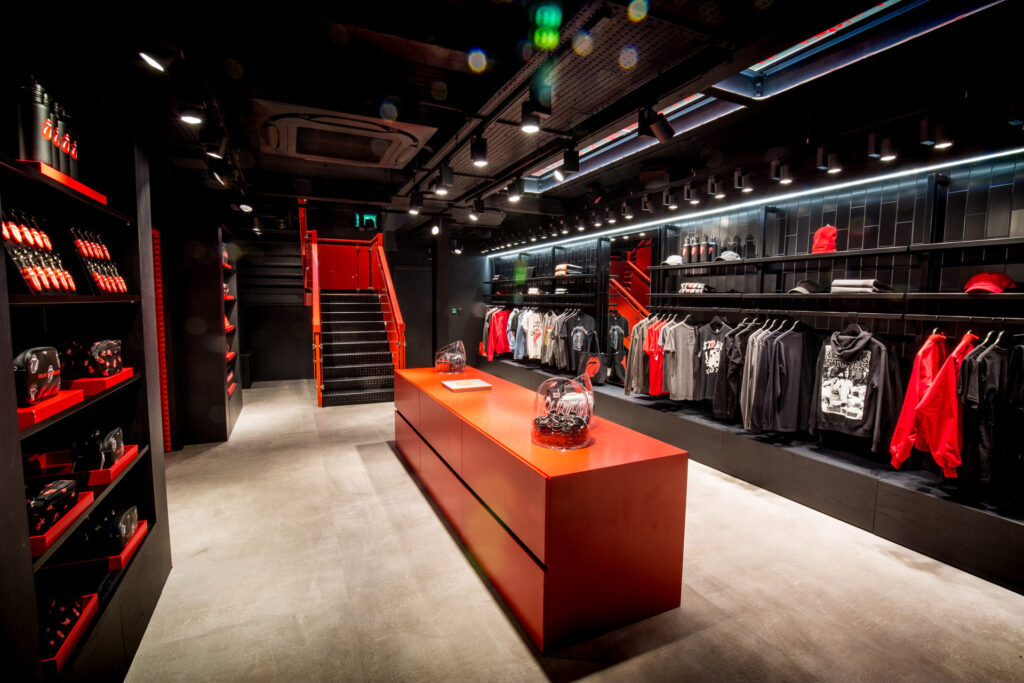 HOL Group A modern retail store with a sleek, dark interior, featuring a long red countertop reminiscent of Rolling Stones' bold aesthetic. Merchandise like clothing and accessories are displayed on the shelves and racks lining the walls. A staircase with a red railing is visible in the background.